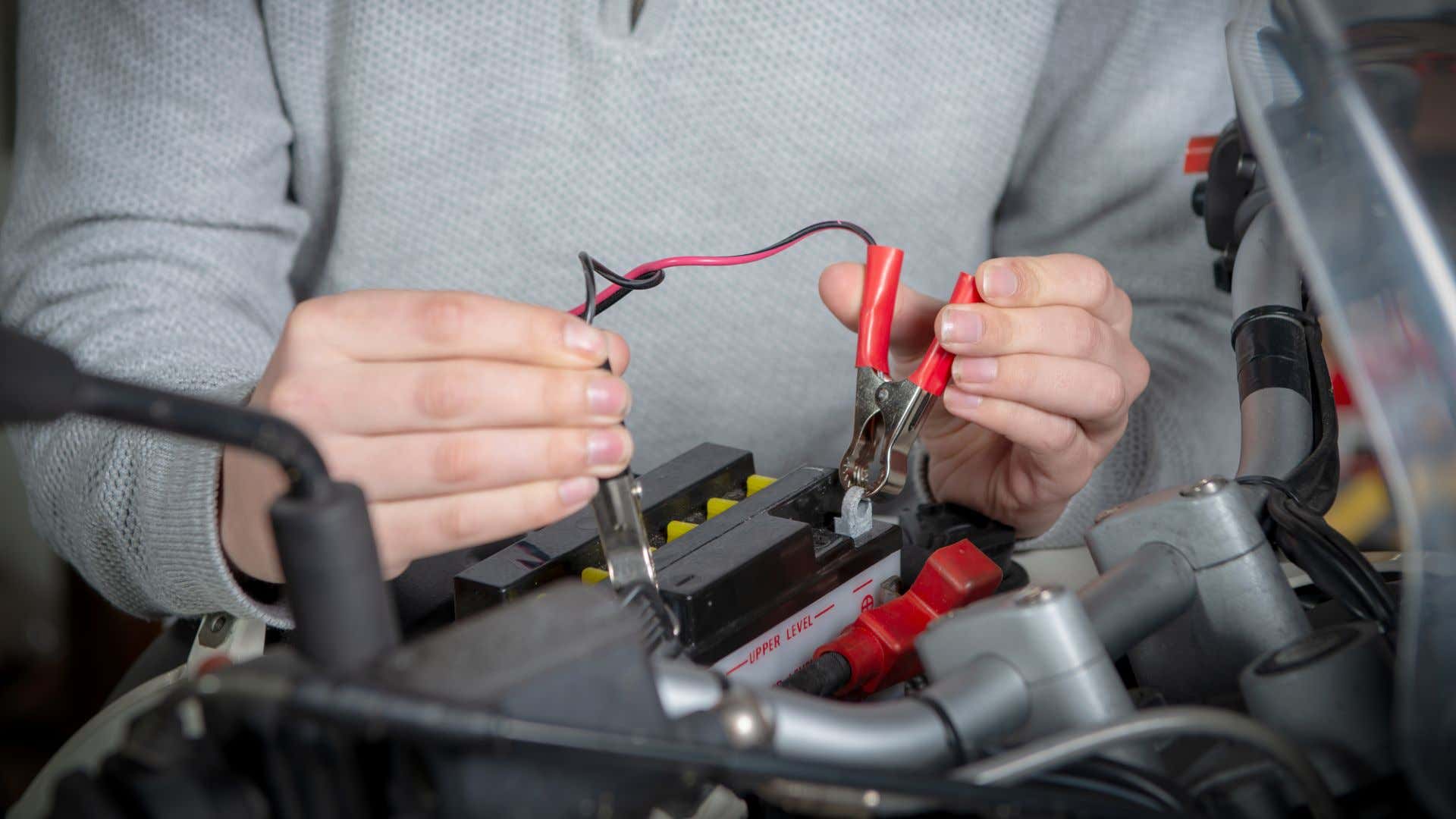 一名男子正在给摩托车电池连接充电电缆。
